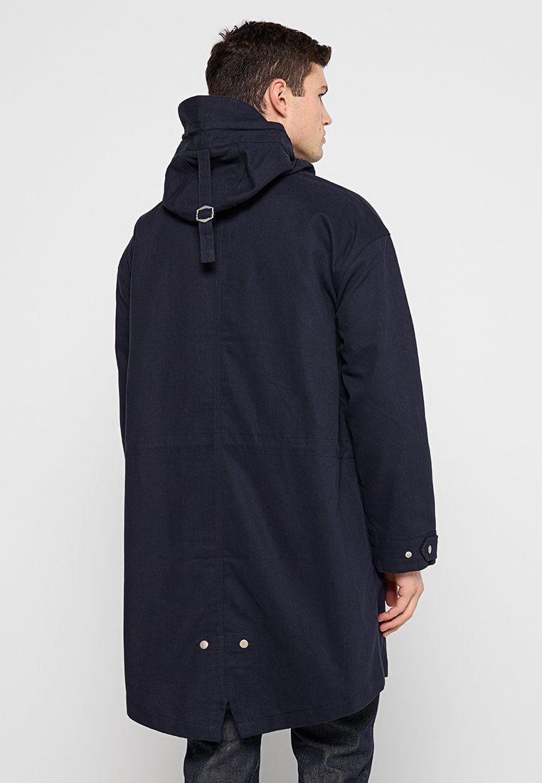 Navy blue wodoodporna parka z kapturem, regulowanym paskiem z tyłu, guzikami przy mankietach oraz bocznymi rozcięciami. Gładka faktura i minimalistyczny design.
