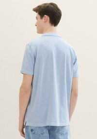 Ljusblå pikétröja med korta ärmar, gjord av slätt tyg, med krage och sidossprund i fållen för ökad rörlighet.