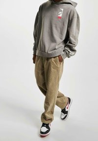 Szara bluza z kapturem z naszywką z logo, zestawiona z beżowymi spodniami sztruksowymi oraz czarno-biało-czerwonymi trampkami, charakteryzująca się luźnym krojem i fakturowaną tkaniną.