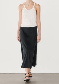 Jupe midi noire fluide avec un léger brillant, dotée d'une taille ajustée et de fentes latérales, associée à un débardeur blanc moulant et des sandales à brides.