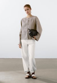 Grijze linnen long sleeve top met knoopdetails aan de voorkant, gecombineerd met losse witte broeken en bruine sandaaltjes met banden. Zwarte geweven tas als accent.