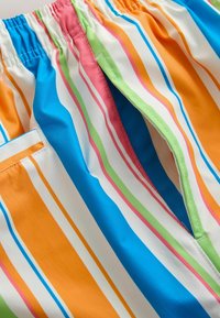 Pantalones cortos con rayas de colores que incluyen azul, naranja, rosa, verde y blanco, con una cintura elástica y bolsillos laterales. Textura suave.