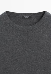 Szara koszulka z okrągłym dekoltem, wykonana z miękkiego, teksturowanego materiału. Posiada metkę z napisem "Massimo Dutti" oraz "Wyprodukowano w Indiach" wewnątrz dekoltu.