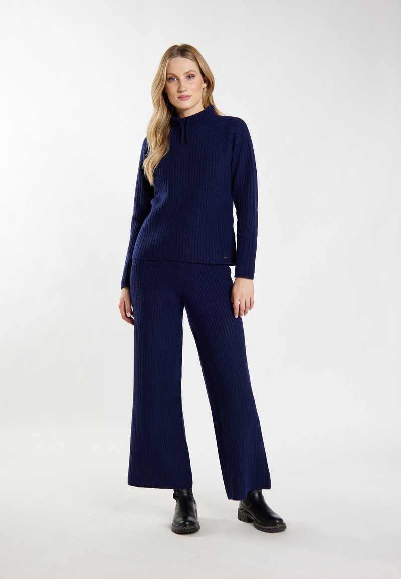 Maglione a costine blu navy con collo alto, abbinato a pantaloni a gamba larga sempre a costine. Texture liscia e dettaglio di branding minimale all'orlo.