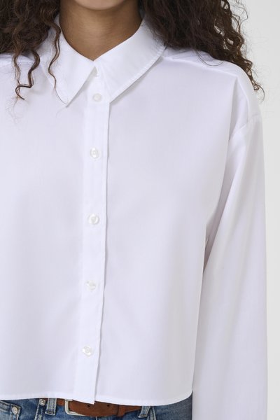 Chemise blanche boutonnée avec un col classique, manches longues et un design court. Tissu lisse avec des boutons effet perle sur le devant.