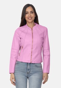 Chaqueta de piel sintética rosa con cuello tipo stand, cremalleras doradas y costuras en ángulo. Diseño ajustado, longitud corta y bolsillos laterales.