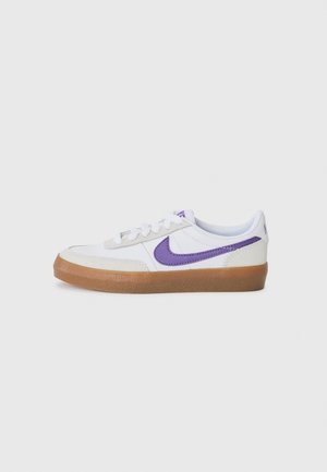 Biały niski sneaker z fioletowym znakiem Nike i gumową podeszwą, widoczny z boku na jasnym, jednolitym tle.