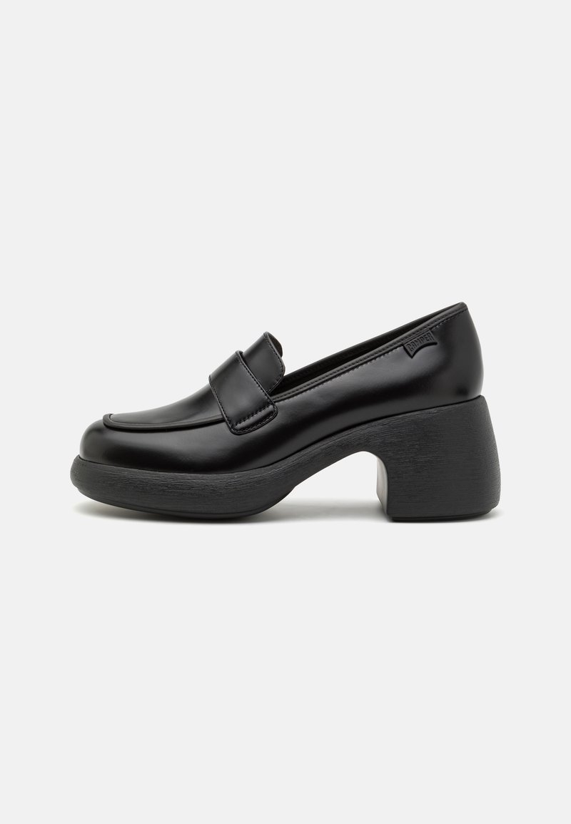 Mocassin en cuir noir avec un talon bloc épais et une large bande sur le devant, présenté sur un fond neutre.