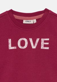 Mörkröd sweatshirt med ribbat runt halsen som har ordet "KÄRLEK" i vita texturerade bokstäver. Mjukt tyg med en avslappnad design.