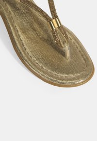 Goldene, glitzernde Flip-Flop-Sandale mit einem strukturierten Fußbett, dünnen Riemen und einem zentralen Metallelement. Verfügt über eine flache Gummisohle.