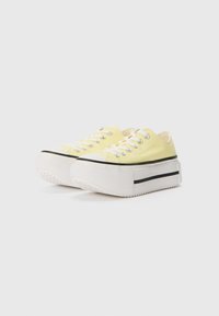 Yellow canvas sneakers with white rubber soles, black stripe detail, and silver eyelets. Low-top design, round toe, and textured outsole.