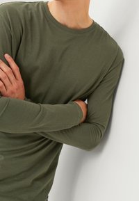 Olivegrünes Langarm-T-Shirt aus weichem Stoff, mit Rundhalsausschnitt und taillierter Silhouette.