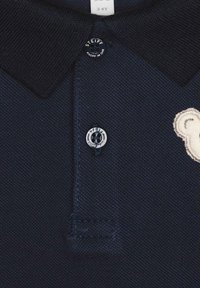 Marineblauwe polo met een gestructureerde stof, met een donkere kraag, een ronde logoknop en een geborduurde berenontwerp aan de voorkant.