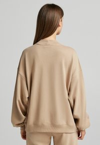 Felpa beige over-size con spalle scese, colletto e polsini a coste. Tessuto morbido con texture minima, caratterizzata da una vestibilità comoda.