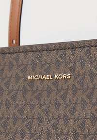 Sac à main texturé en brun avec le logo doré "MICHAEL KORS", doté d'un motif et d'accents en cuir lisse.