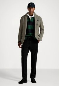 Švarkas iš eglutės rašto audinio, žaliai ir tamsiai mėlyna dryžuota polo marškinėliai, juodos kelnės, juodi sportbačiai ir juoda kepurė su logotipu.