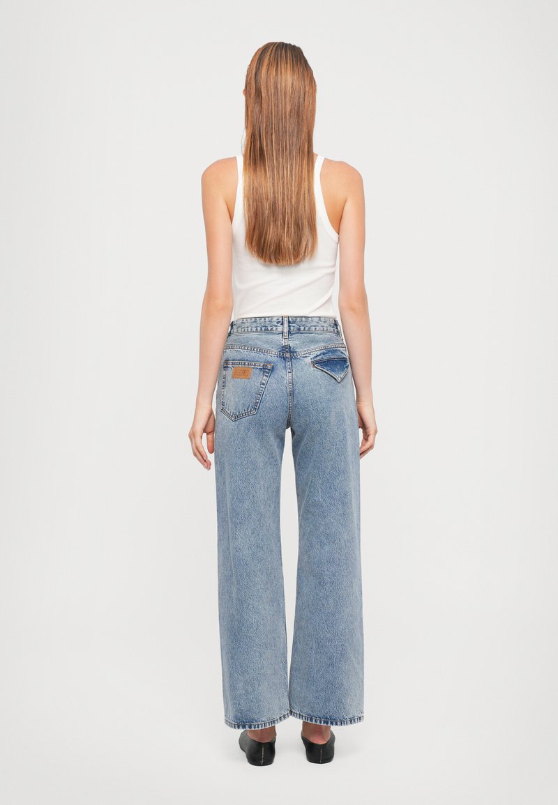 Jeans bleus évasés en denim délavé avec une taille haute. Présente deux poches arrière et une étiquette en cuir sur la taille. Ourlet plat.