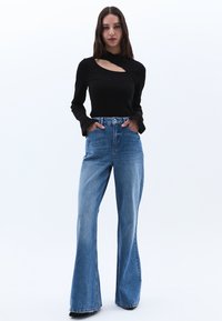 Musta pitkähihaisuus yläosa, jossa on leikkauksellinen yksityiskohta, yhdistettynä vaaleansinisiin korkea vyötäröisiin väljään farkkuihin. Tasainen kangasmateriaali.