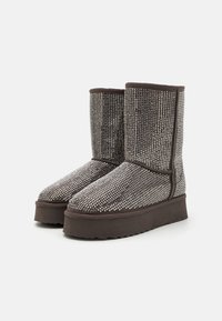 Brune ankelstøvler med en teksturert overdel med metallisk detaljering, høy skaft og en tykk, rasset såle for ekstra støtte.