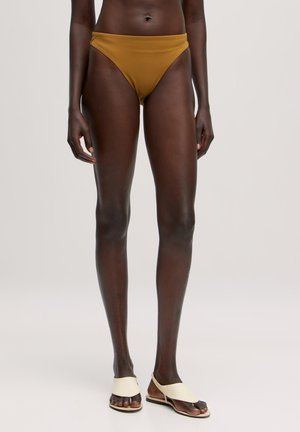 Bruine bikini-onderkant met een hoge snit, gladde textuur en minimalistische stijl. Gepaarde met crème flat sandals met een gespleten band.