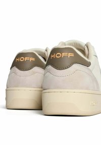 Witte sneakers met beige suède accenten, voorzien van een tan leren hieltab met de opschrift "HOFF." Rubberen zool met een getextureerde afwerking.