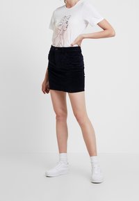 Vitt t-shirt med en minimalistisk linjeteckning, kombinerat med en mörkblå manchesterkjol, kompletterat med vita sneakers och ankelsockor.