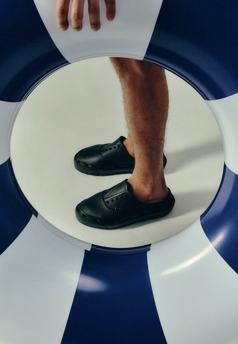 Main tenant une bouée de sauvetage bleue et blanche avec les jambes d’une personne et des chaussures noires sans lacets visibles à travers l’ouverture centrale.