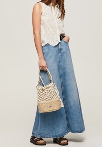 Blouse sans manches de couleur claire avec des détails en dentelle; associée à une longue jupe en denim; tenant un sac en macramé tissé; sandales noires.