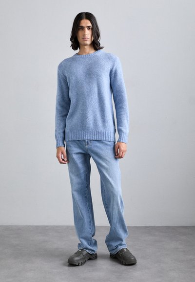 Light blue knitted sweater with a rounded neckline, ribbed cuffs, and hem. Paired with light blue denim jeans and dark casual shoes.