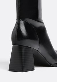 Schwarze Leder-Ankle Boots mit quadratischer Zehenform und einem klobigen, gerippten Absatz. Die Oberfläche ist glatt mit einem glänzenden Finish.
