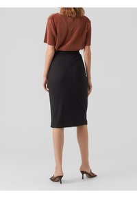 Haut côtelé en rouille associé à une jupe crayon noire ajustée. La jupe présente une texture subtile. Des sandales à talons strappy beiges complètent le look.