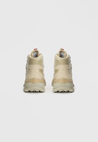 Un par de zapatillas altas beige de espaldas sobre un fondo blanco, con suelas texturizadas y cuellos acolchados.