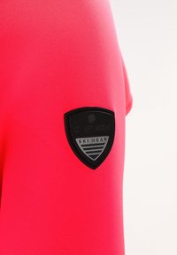 Tessuto di un rosa acceso con una toppa a forma di scudo nera e argento con la scritta "ICEPEAK SKI WEAR" nella zona superiore del braccio.