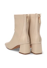Botines beige hasta el tobillo con un acabado de cuero suave, tacones en bloque y cremalleras laterales dobles. Diseño minimalista con una sutil marca en el tacón.