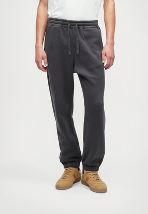 Gray cotton sweatpants with an elastic waistband, adjustable drawstring, and cuffed hems, paired with tan sneakers.