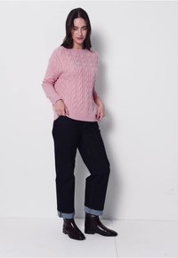 Jasnoróżowy sweter z dzianiny o splocie warkoczowym, zestawiony z ciemnoniebieskimi dżinsami z zakładkami i błyszczącymi czarnymi botkami na kostkę. Prosty, teksturowany fason.