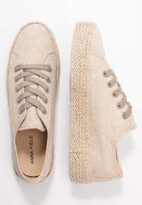 Beiga kanvas sneakers med en flätad jutesula, rund tå och sex hål med ljusgrå snören. Varumärket syns inuti.