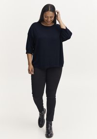 Luźny, granatowy sweter z dzianiny z rękawami do łokcia, w zestawieniu z czarnymi dopasowanymi spodniami i czarnymi botkami za kostkę. Prosty design, bez wzorów.