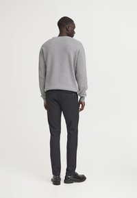 Sivi pleteni pulover, temne uske hlače, črne čevlje. Mehak material, kroj s krožnim izrezom, z diskretnim vzorcem na puloverju in dvema zadnjima žepoma na hlačah.