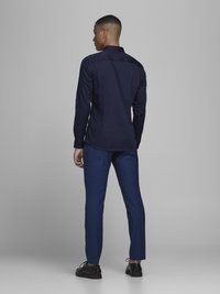 Navy long-sleeve shirt with buttoned cuffs, paired with tailored blue pants and black shoes. Smooth fabric and slim fit design.