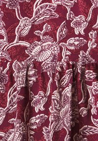 Tessuto bordeaux con intricati motivi floreali bianchi, caratterizzato da foglie sovrapposte e una cucitura gathered nella parte inferiore.