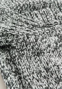 Strickschal in Schwarz, Weiß und Grau mit einer groben Textur. Verfügt über eine lockere Webart und ein geflochtenes Muster.