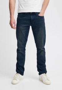 Mørkeblå jeans laget av denimstoff, med en tettsittende design, standard fem-lommers stil, og subtil whiskering på lårene.