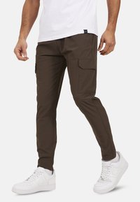 Brązowe spodnie cargo z bocznymi kieszeniami, slim fit oraz lekkiego materiału. Połączone z białymi trampkami o teksturowej powierzchni.