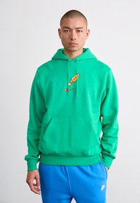 Grøn hættetrøje lavet af bomuld, med en frontlomme og et grafik af en flaske på brystet. Sammen med blå sweatpants.