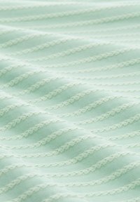 Licht muntgroene stof met gestructureerde golfpatronen en fijne, afwisselende witte ruches. Zacht, glad oppervlak met een subtiele glans.