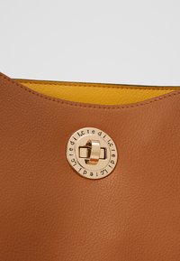 Bolso de mano de cuero marrón con un interior amarillo, parte superior curvada y un cierre circular en tono dorado con detalles de marca grabados.