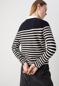 Tengerészkék és krémszínű csíkos pulóver, kerek nyakkivágással és hosszú ujjakkal, amelynek hátulja egyszínű és sima kötött textúrája van.