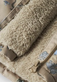 Veste en polaire beige, doublée et au toucher doux, ornée de motifs animaliers ludiques et dotée d'une fermeture éclair visible, le tout sur un fond de tissu tan.