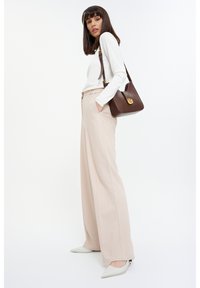 Beige weite, hochtaillierte Hose, kombiniert mit einem weißen Langarmoberteil und einer braunen Leder-Crossbody-Tasche. Spitz zulaufende weiße Absätze.